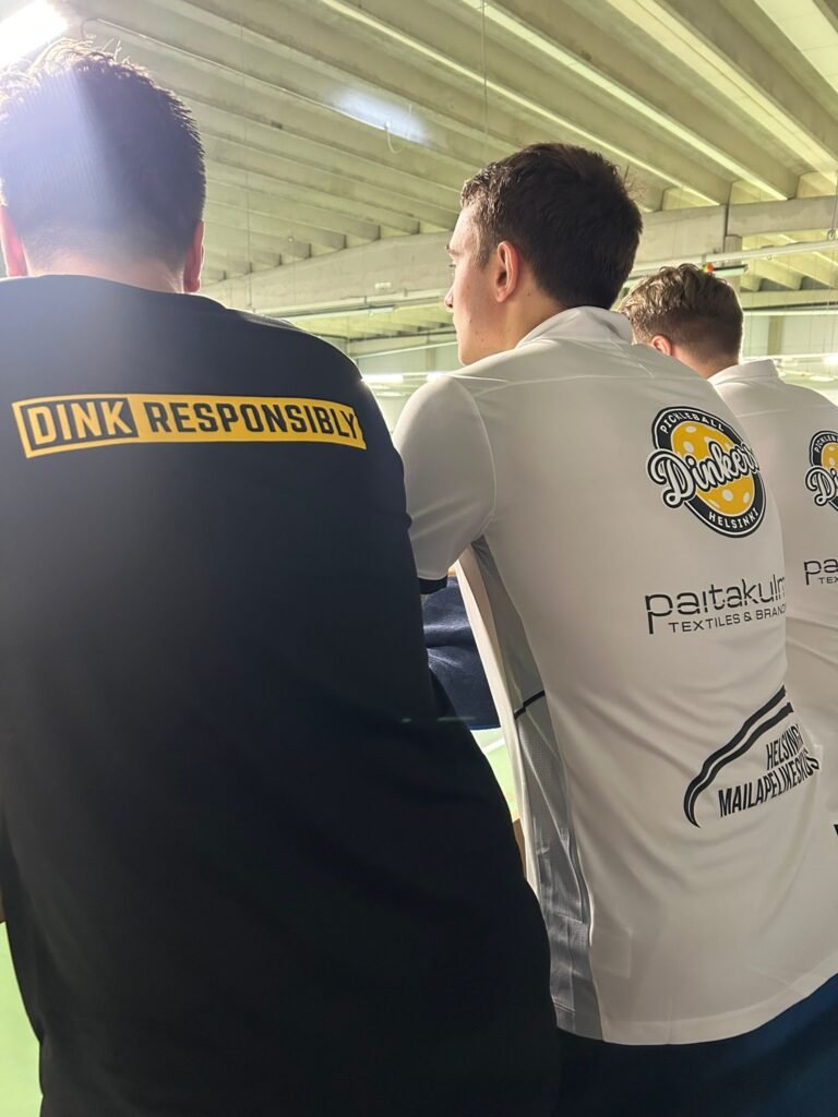 Pelaajat nojaavat kaiteeseen katsomassa pickleball-peliä Helsingissä